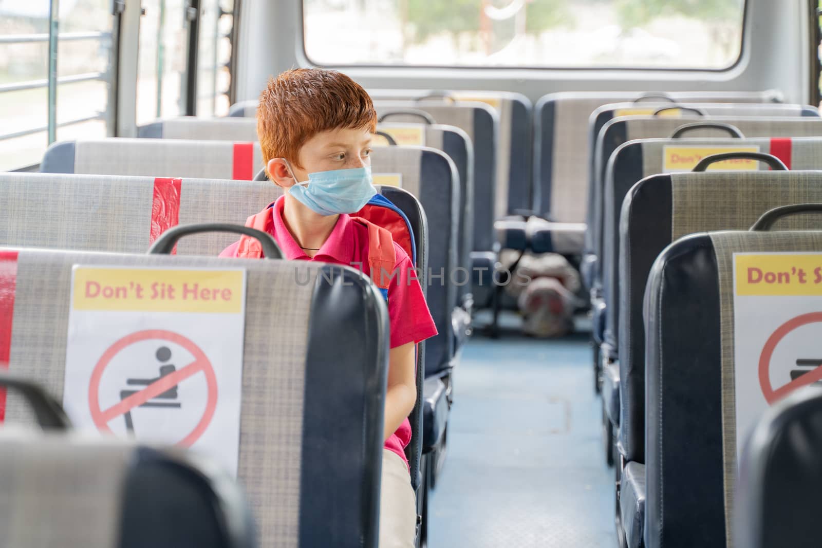 Kid medical mask sitting inside school bus while maintaining social distance due to coronavirus or covid-19 pandemic - Concept of school reopen or back to school.