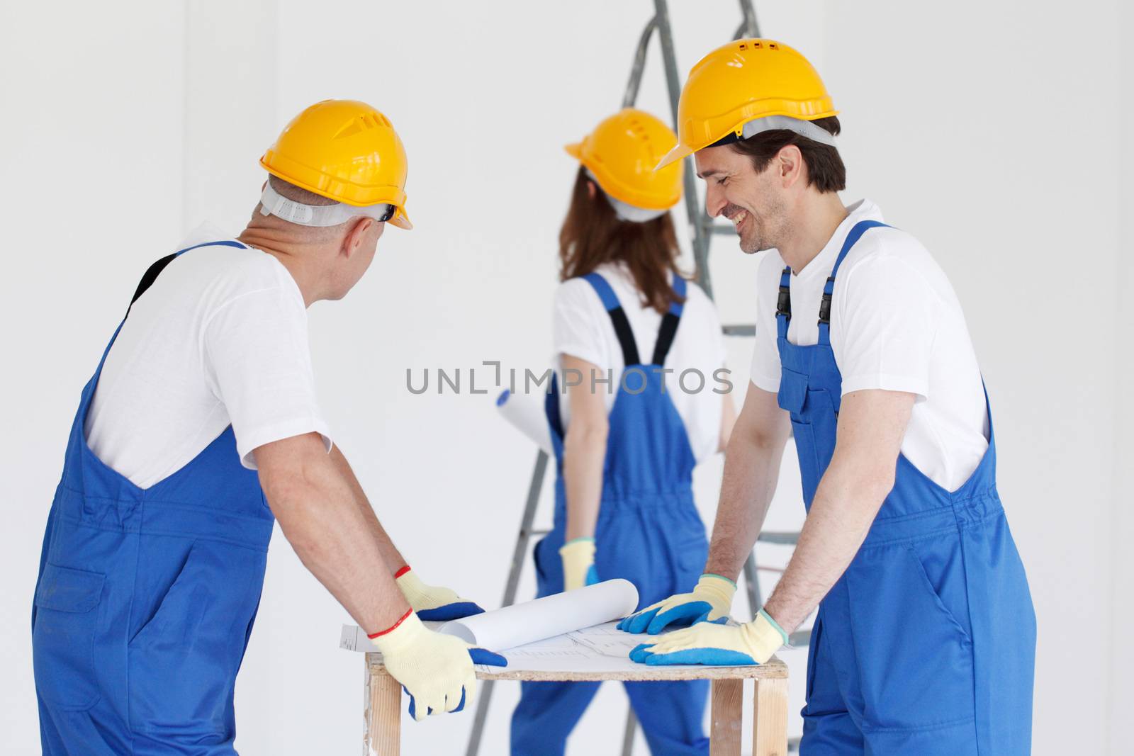 Workers in blue uniform and yellow hardhats with blueprint working at construction site