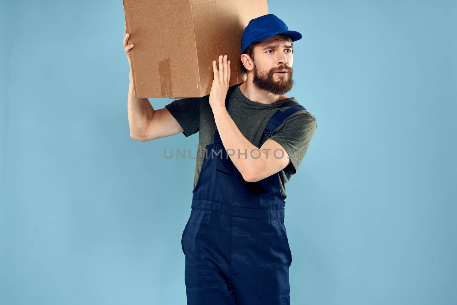 A man in working uniform with boxes in the hands of a carriage delivery service blue background by SHOTPRIME