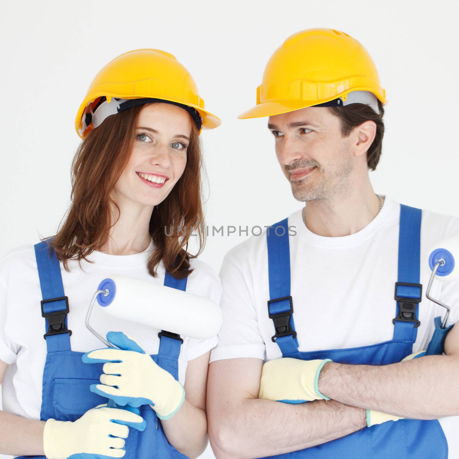 Two young workers in uniform of coverall and hardhat with paint rollers