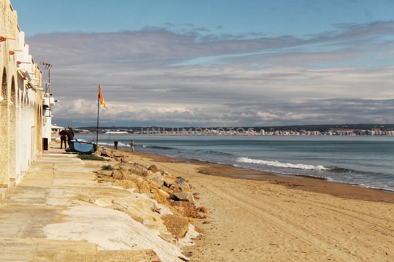 Alicante, Spain- March 7, 2018: Fishing boats under spanish flag and people chatting on the shore in the morning