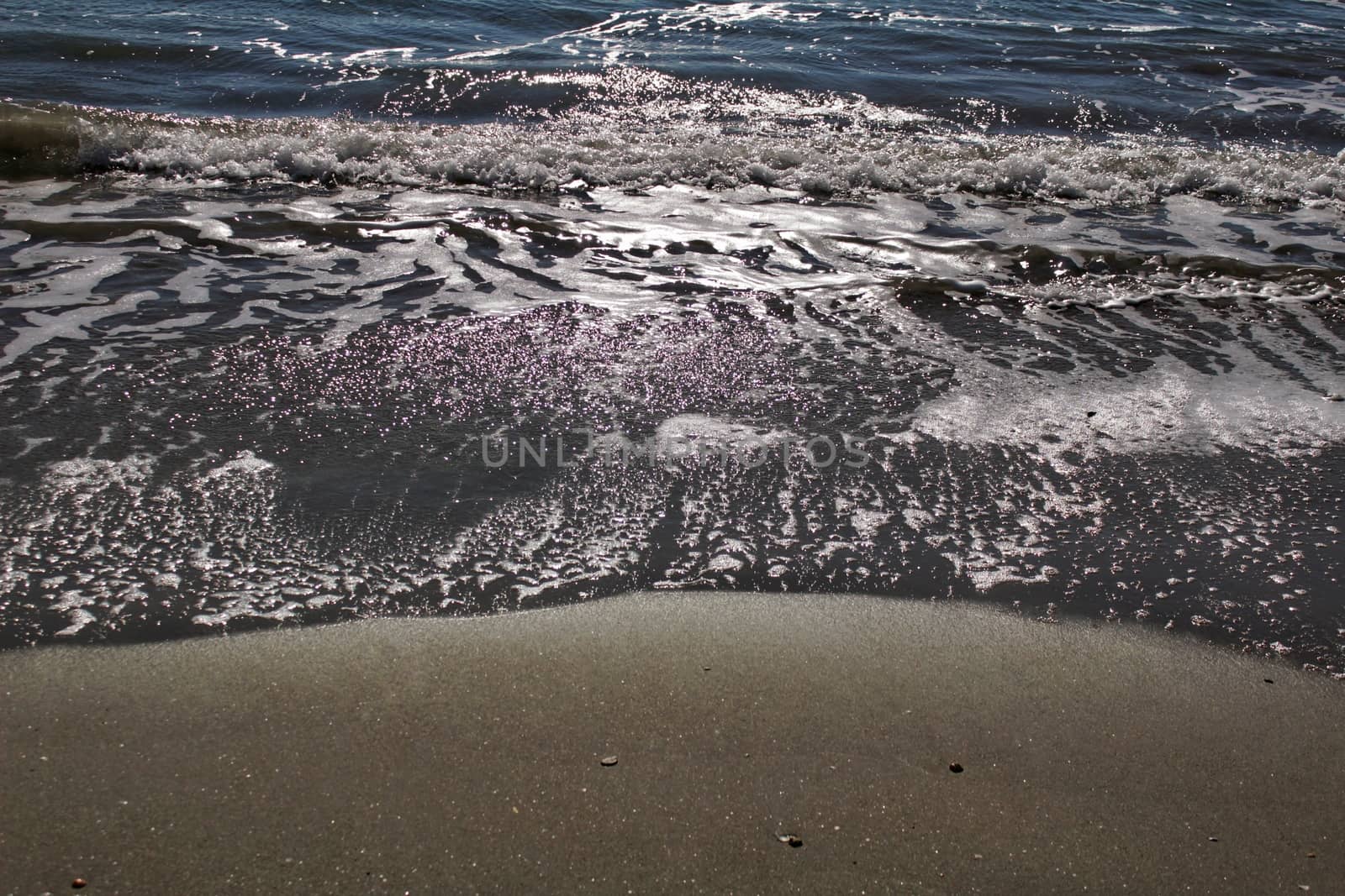 Waves, light and sand texture on the beach in the morning