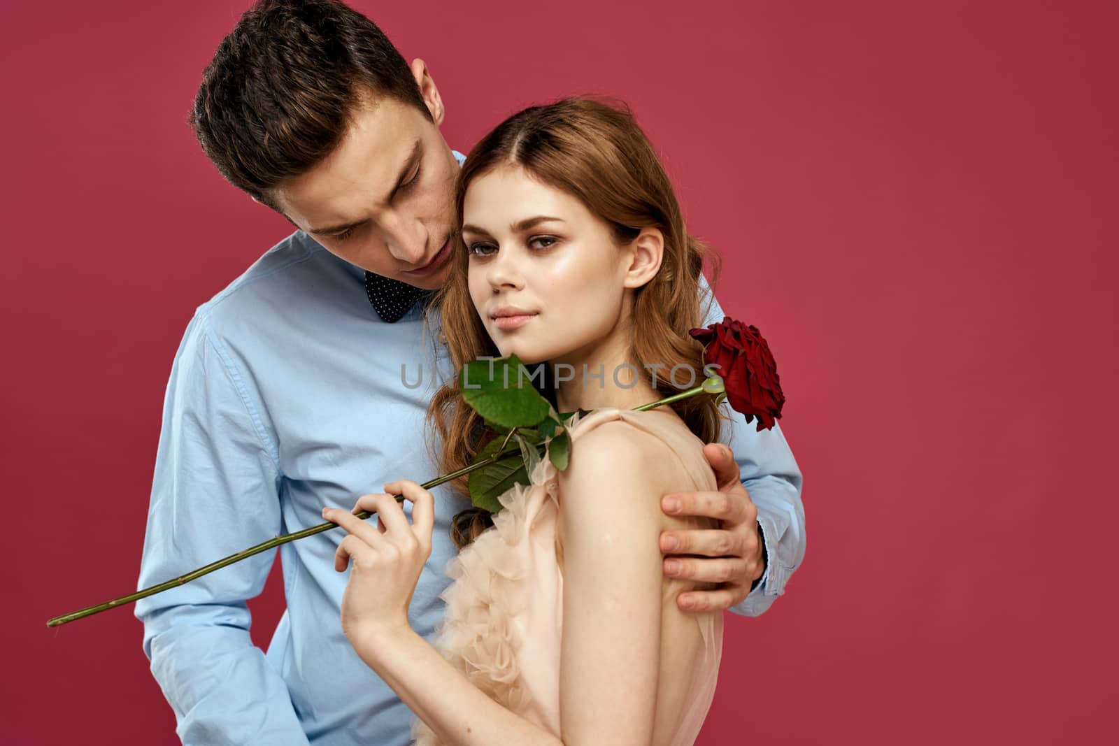 enamored man and woman with a red flower on a pink background hug each other Copy Space by SHOTPRIME