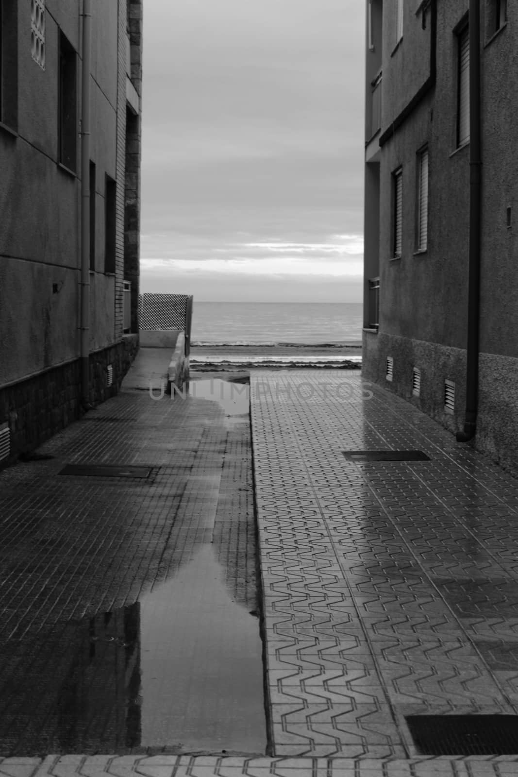 Lonely Little street between buildings facing the sea after a rainy day. Black and white Photography