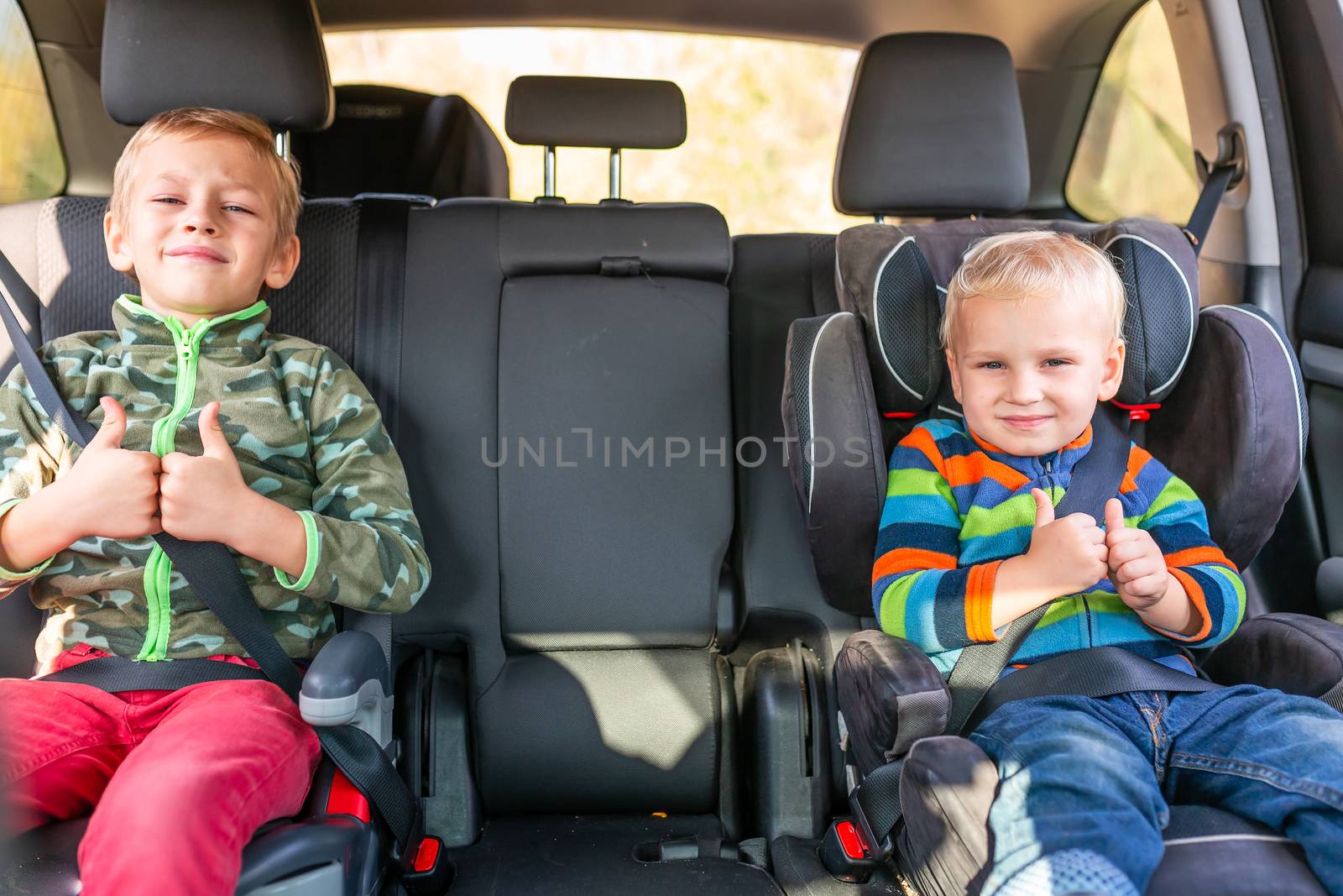 Two little boys sitting on a car seat and a booster seat buckled up in the car. Children's Car Seat Safety