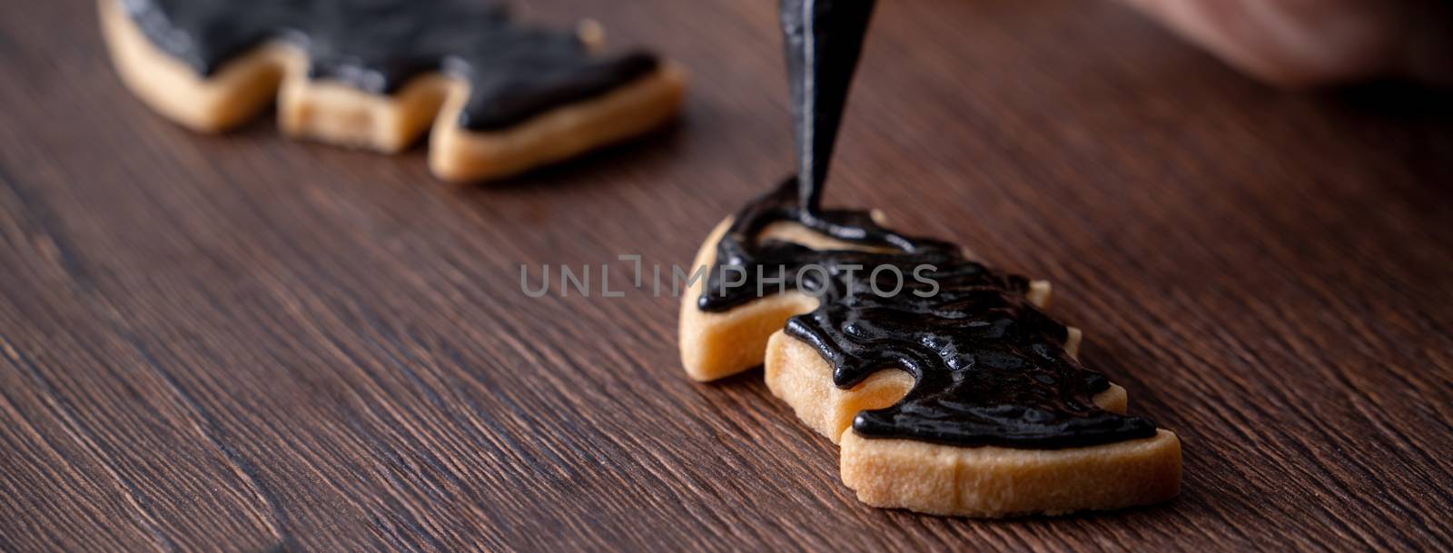 Close up of decorating cute Halloween bat gingerbread sugar cookies with frosting icing cream topping bag.