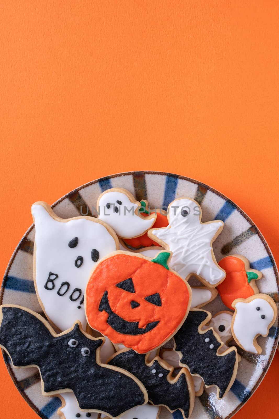 Top view of Halloween festive decorated icing gingerbread sugar cookies on orange background with copy space and flat lay layout.