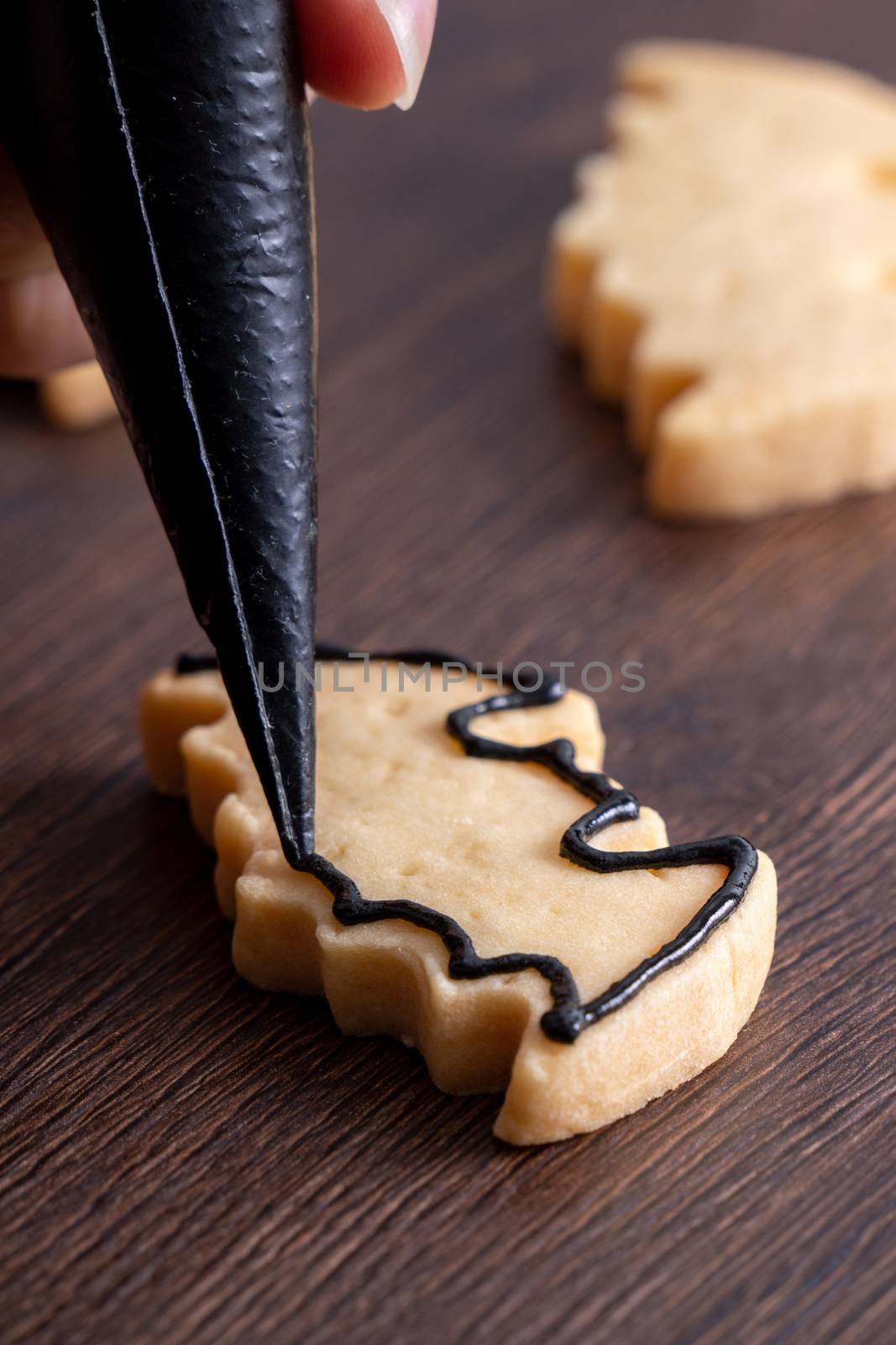 Close up of decorating cute Halloween bat gingerbread sugar cookies with frosting icing cream topping bag.