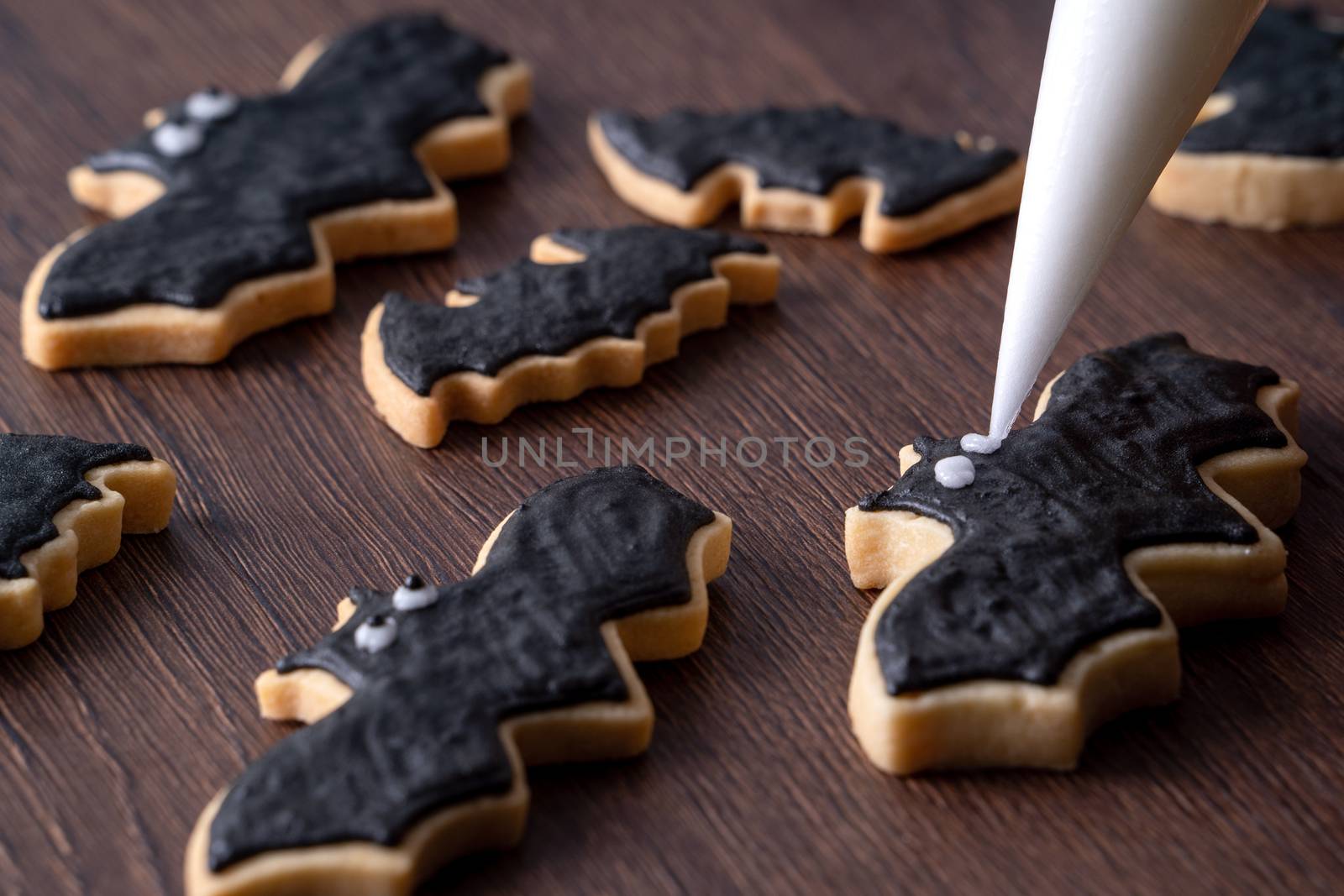 Close up of decorating cute Halloween bat gingerbread sugar cookies with frosting icing cream topping bag.