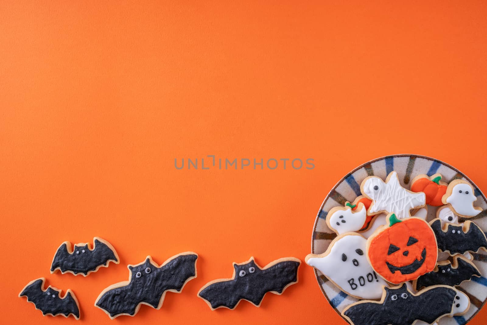 Top view of Halloween festive decorated icing gingerbread sugar cookies on orange background with copy space and flat lay layout.