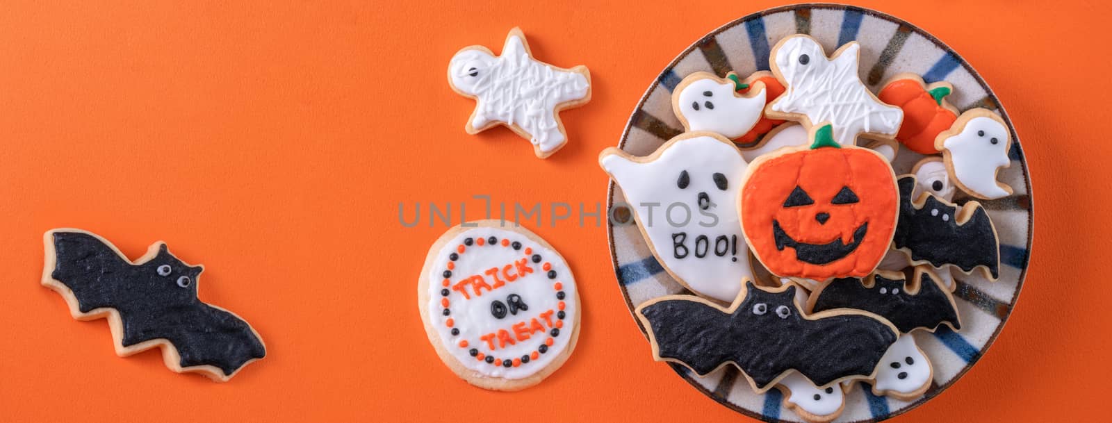 Top view of Halloween festive decorated icing gingerbread sugar cookies on orange background with copy space and flat lay layout.