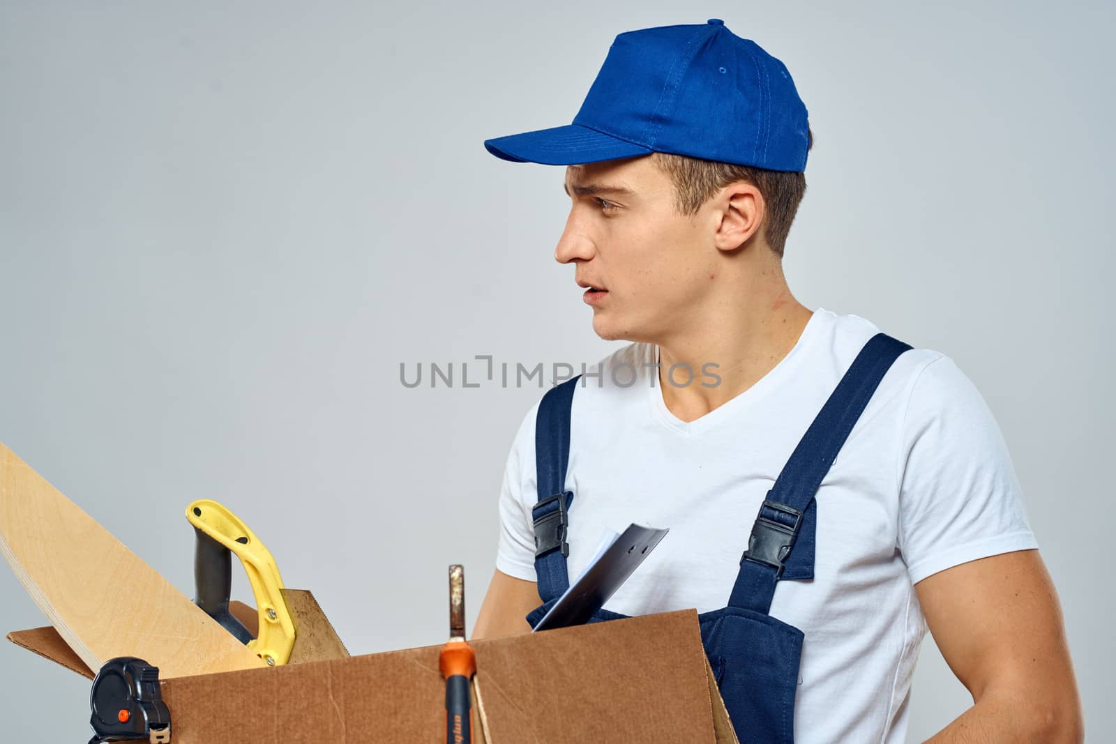 man in working uniform with a box in his hands tools loader delivery light background by SHOTPRIME