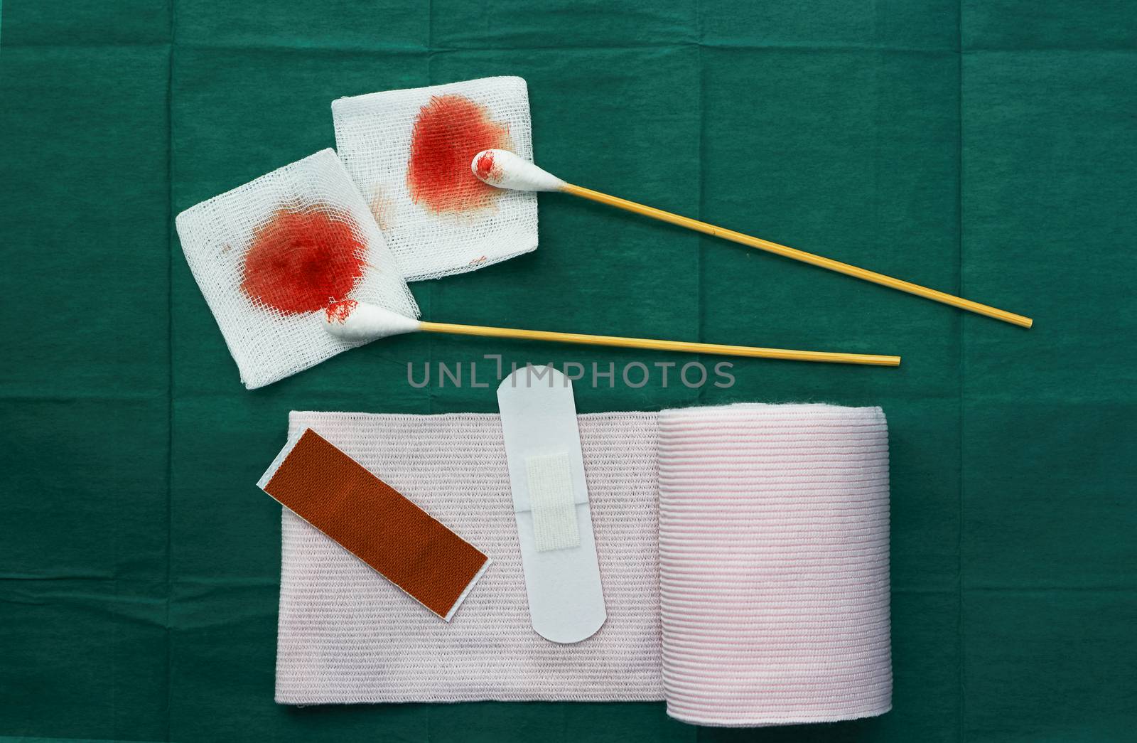 tools include plasters ,swab,roll gauze and blood gauze on green surgical dress  for clean wound