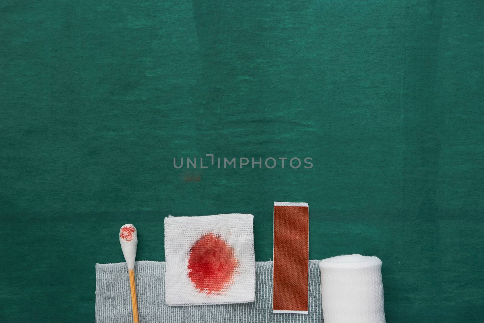 plaster,swab,blood gauze and roll gauze on green surgical dress for clean wound with copy space