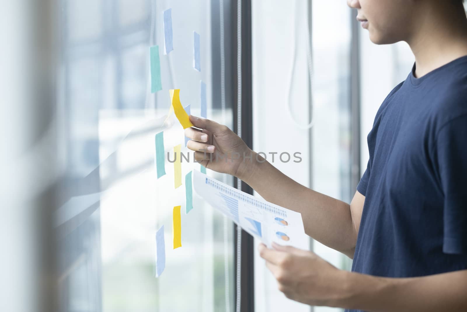 Young creative man reading sticky notes on glass wall.