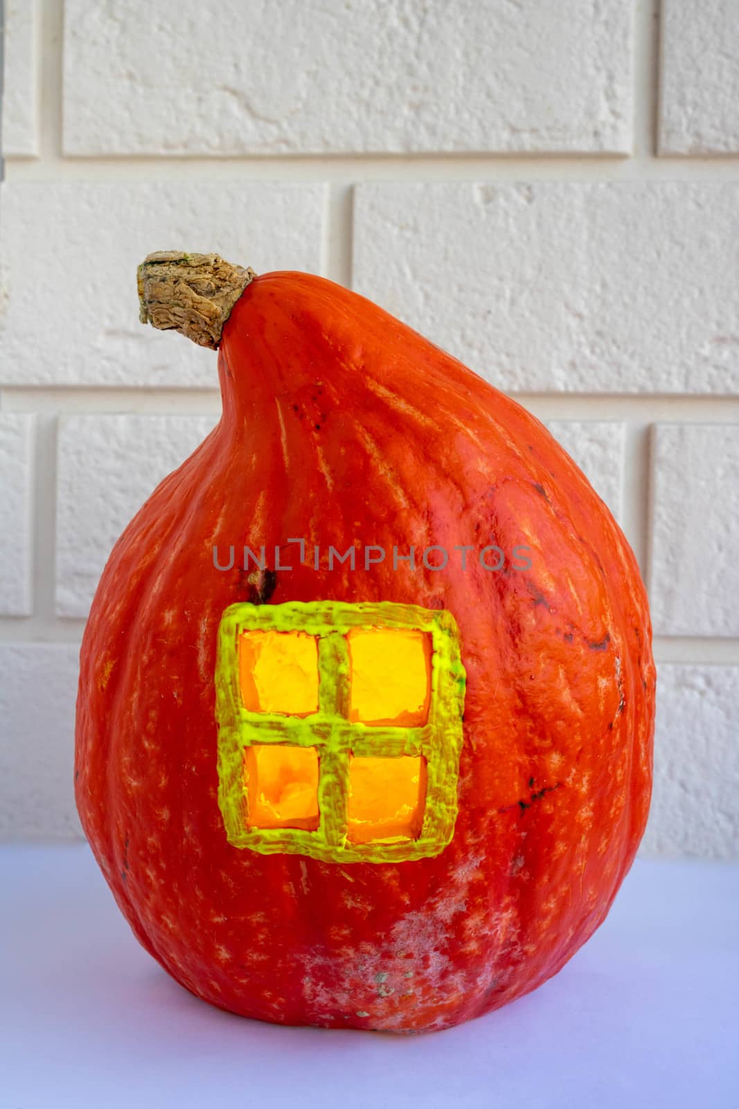 Pumpkin house with a window on a white brick background. The concept of Halloween ,harvest,thanksgiving,vegetarianism by lapushka62