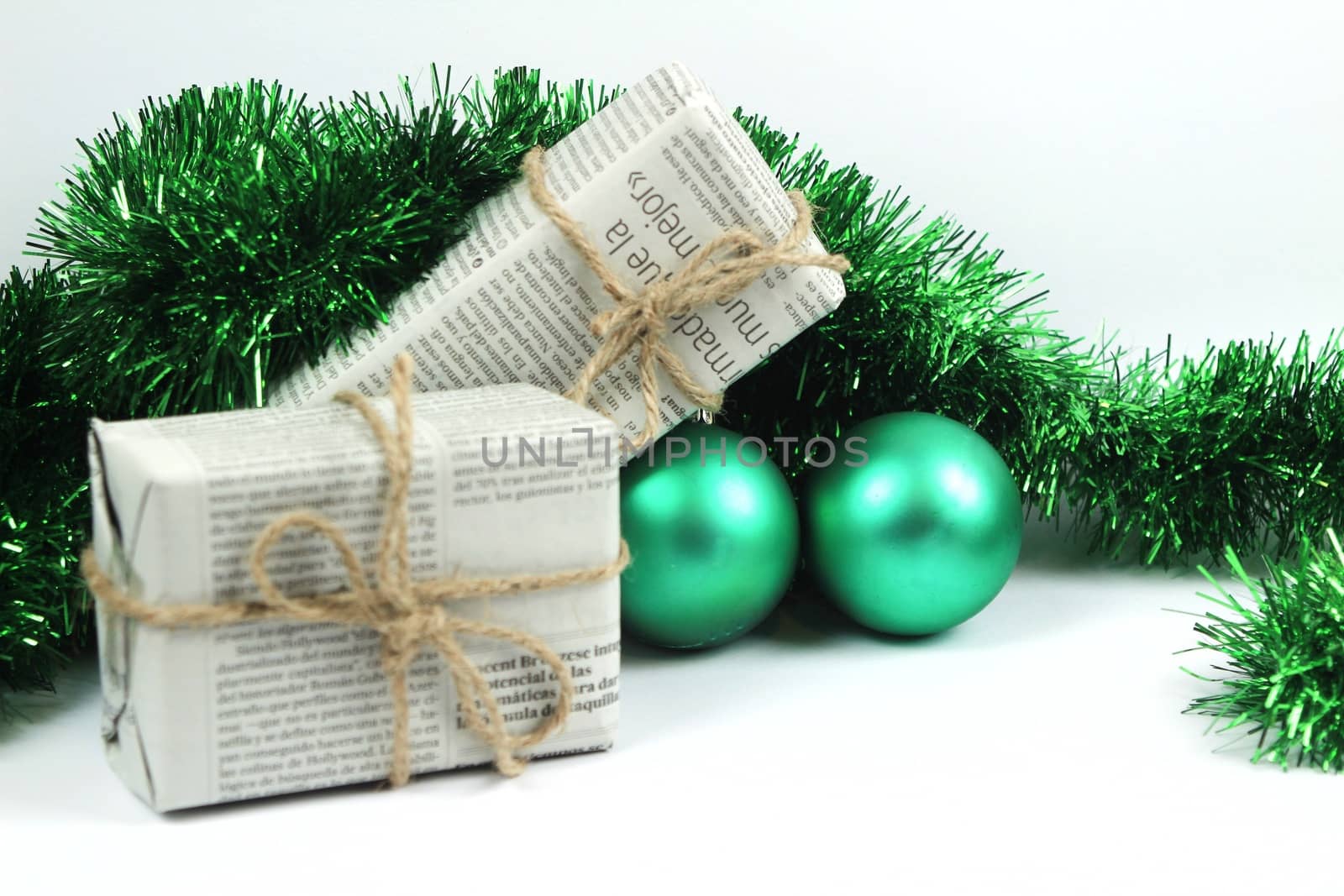 Gifts wrapped in old newspaper with green tinsel, rope and green baubles on white background