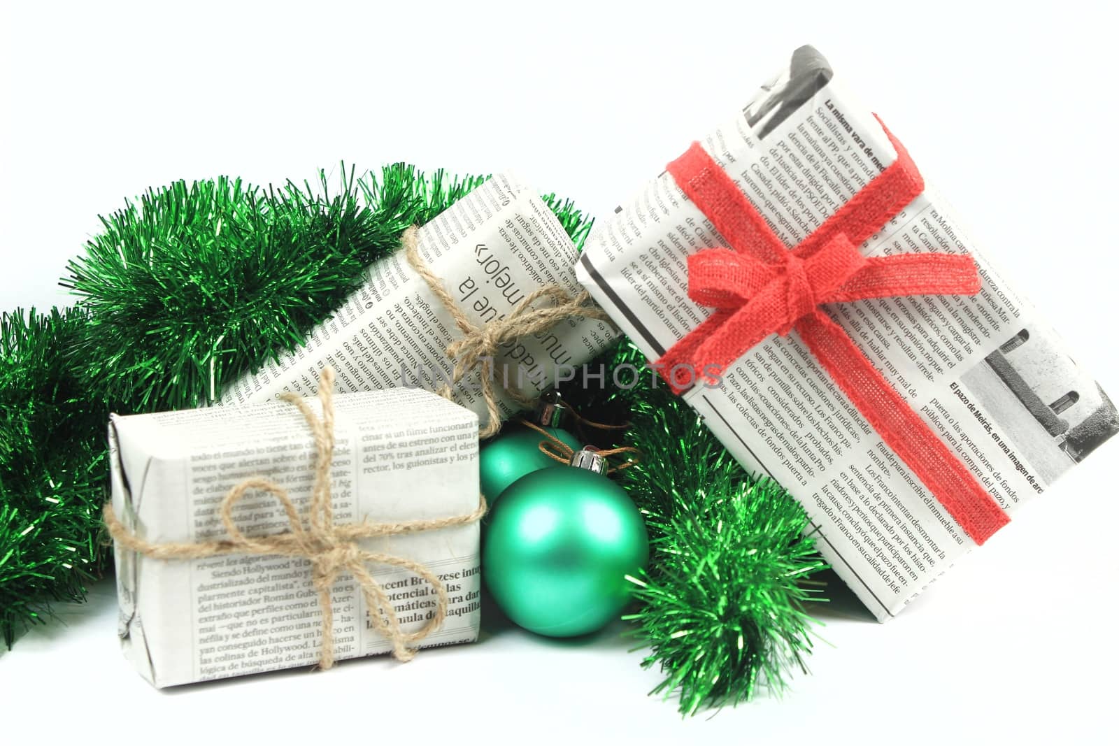 Gifts wrapped in old newspaper with green tinsel, rope and green baubles on white background