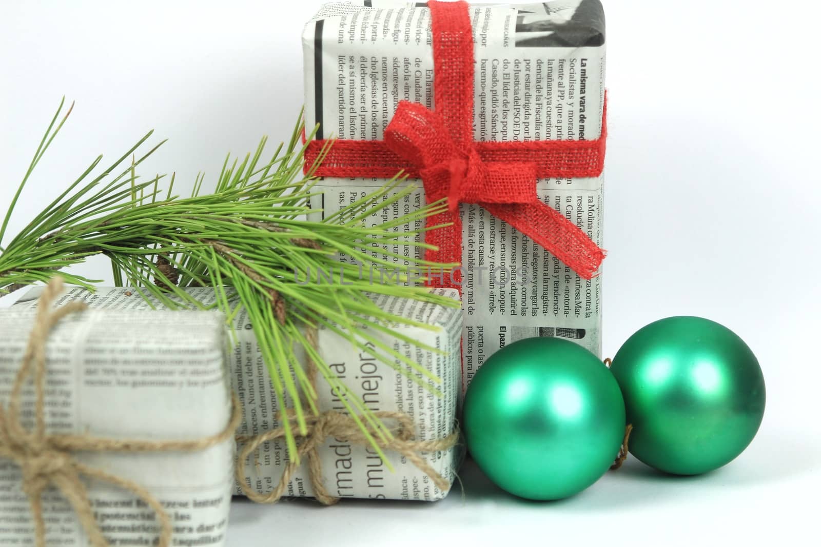 Gifts wrapped in old newspaper with pine branch, rope and green baubles on white background