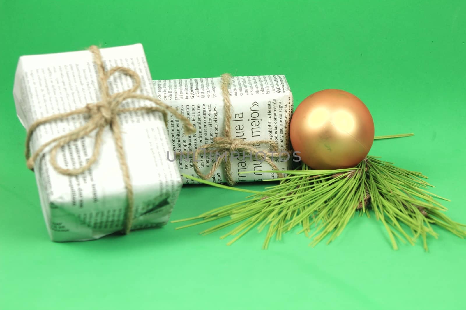 Gifts wrapped in old newspaper with pine branch, rope and golden bauble on green background