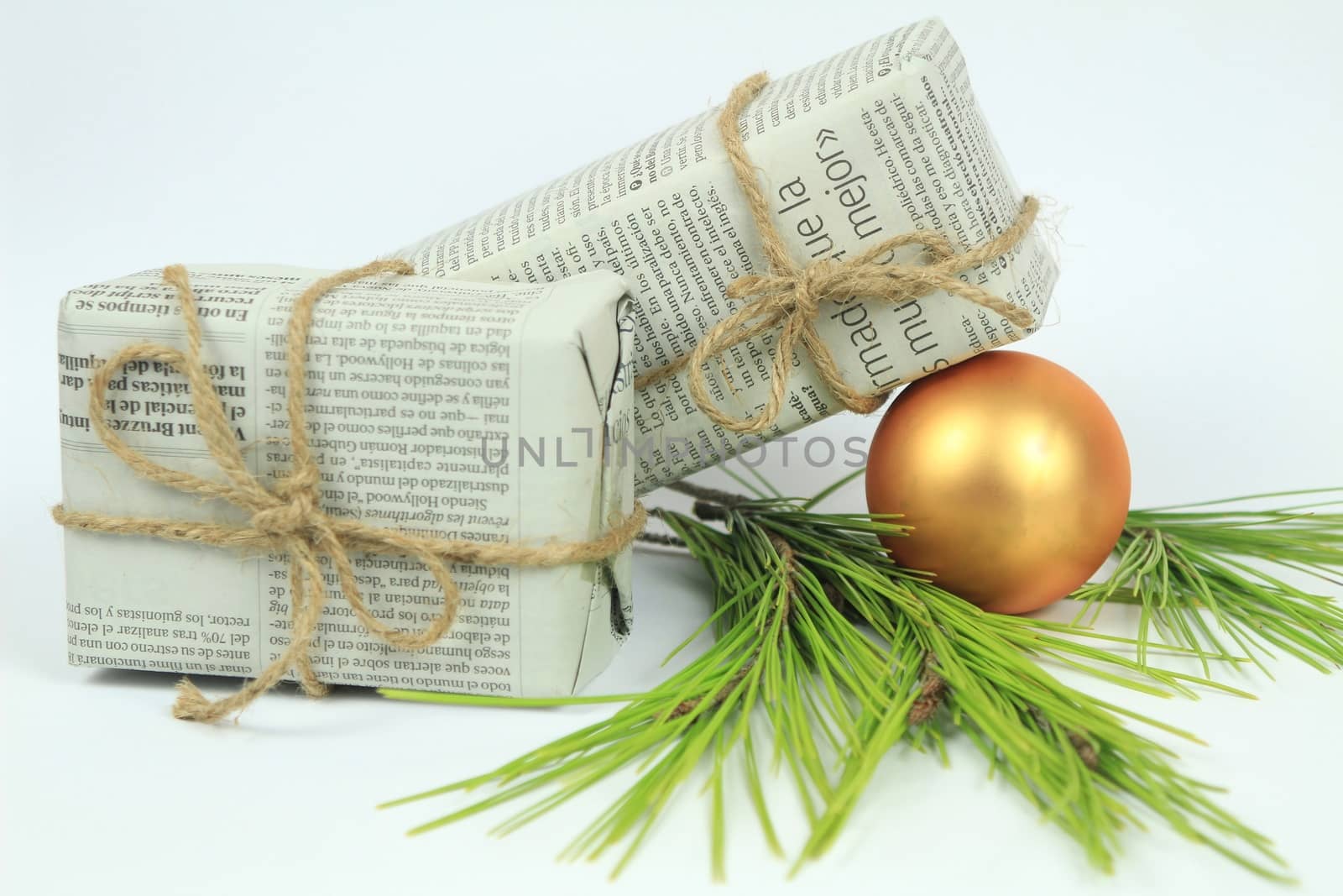Gifts wrapped in old newspaper with pine branch, rope and golden bauble on white background