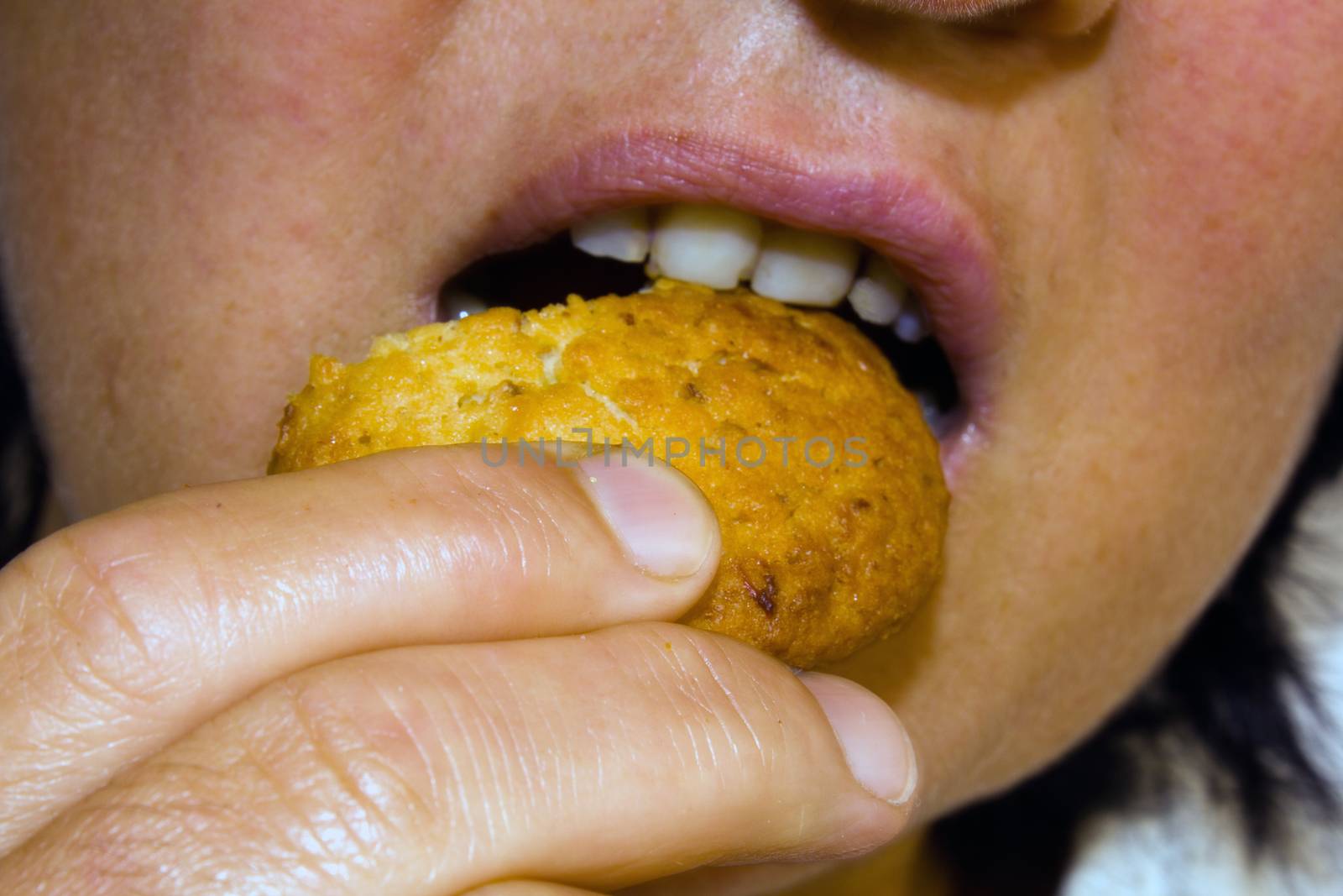 part of the face and hand of a woman holding and eating a cookie