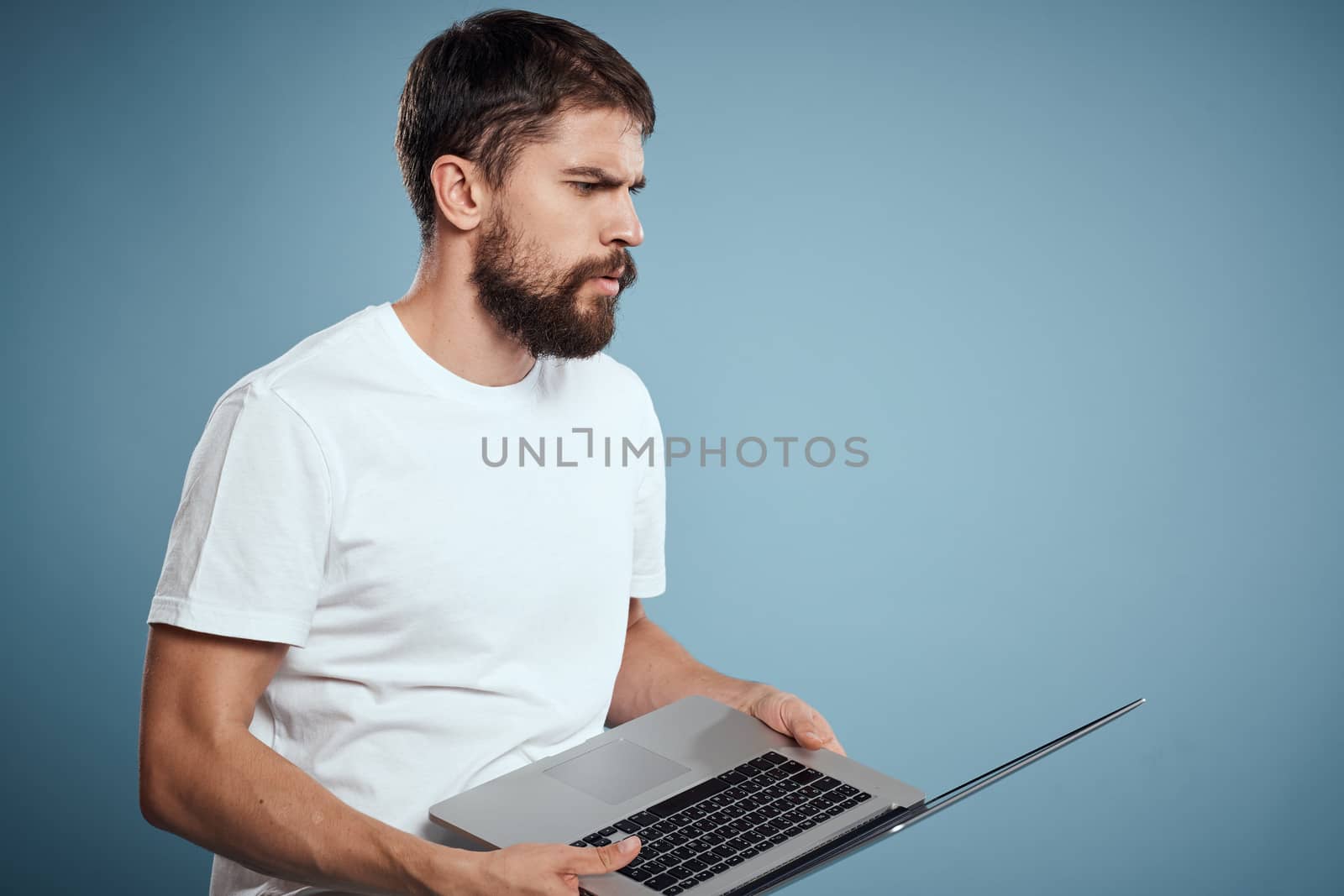 Emotional man with laptop in hands on blue background monitor keyboard internet model cropped view. High quality photo