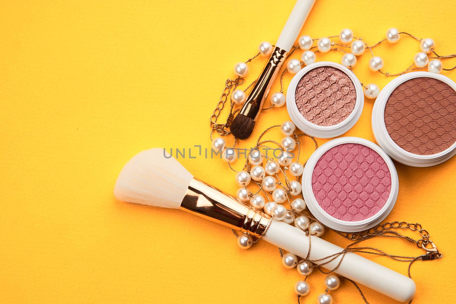 Eyeshadows and makeup brushes on a yellow background top view professional cosmetics by SHOTPRIME