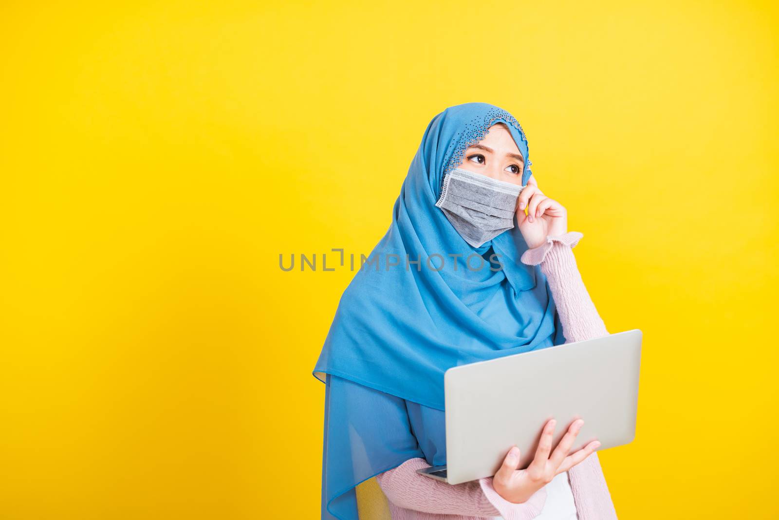 Asian Muslim Arab, Portrait of happy beautiful young woman Islam religious wear veil hijab and face mask protect she quarantines disease coronavirus hold laptop computer and thinking question