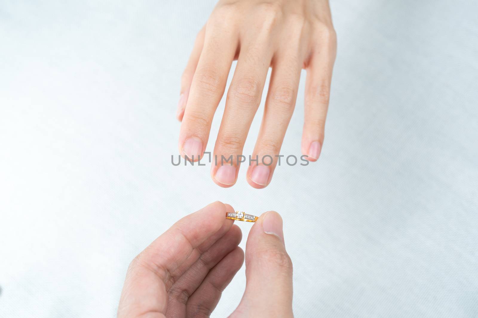 Man putting diamond ring on woman hand over white background.