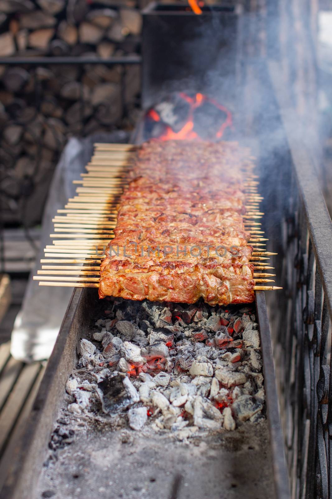 A lot of kebabs in a row on the grill. Kebabs strung on wooden skewers in a street cafe. The process of cooking kebabs with a lot of smoke.