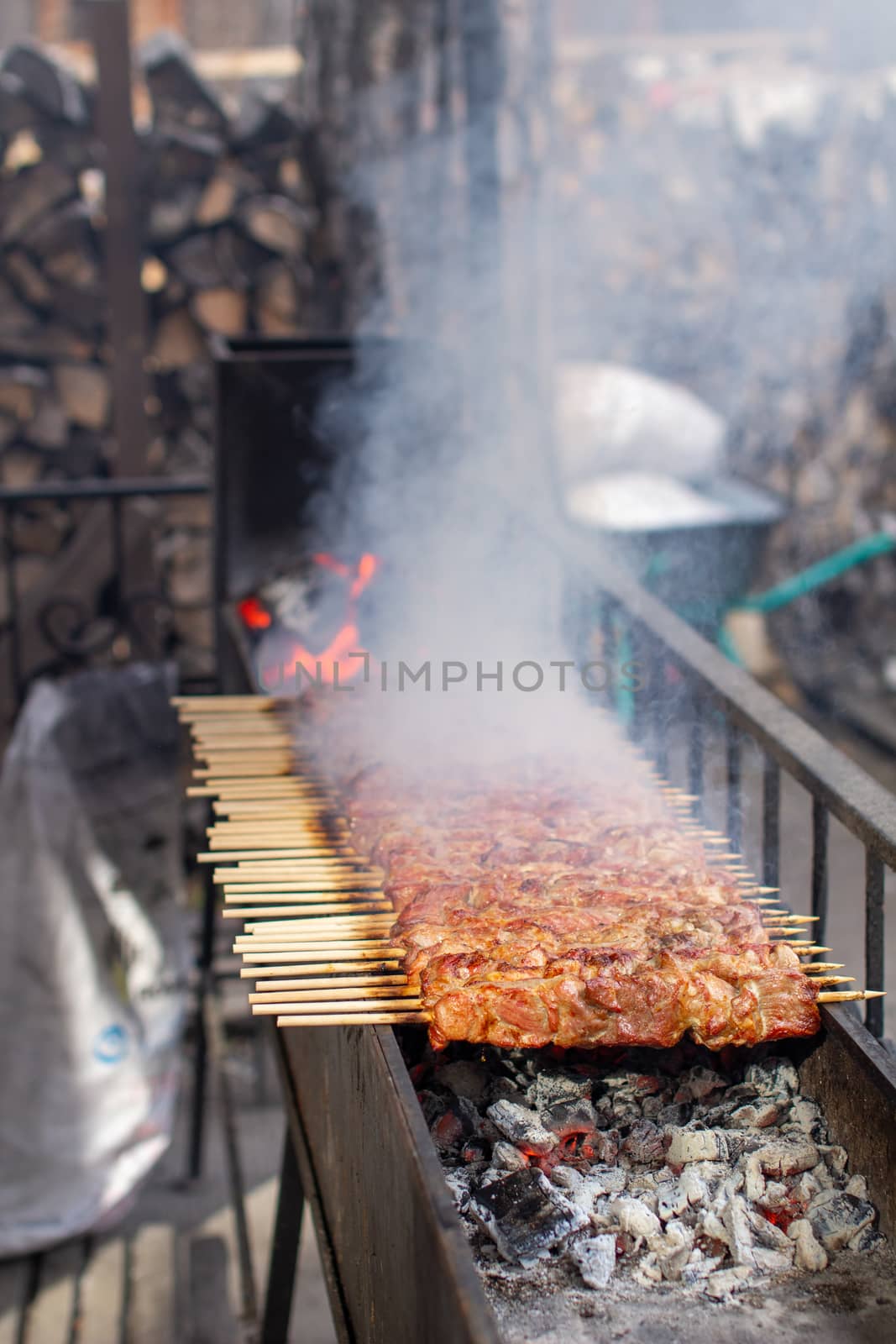 A lot of kebabs in a row on the grill. Kebabs strung on wooden skewers in a street cafe. The process of cooking kebabs with a lot of smoke.