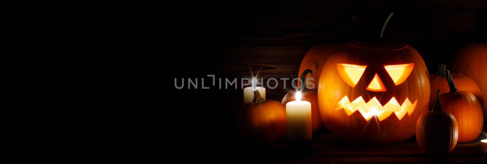 Halloween pumpkin head lanterns and burning candles on wooden background isolated on black