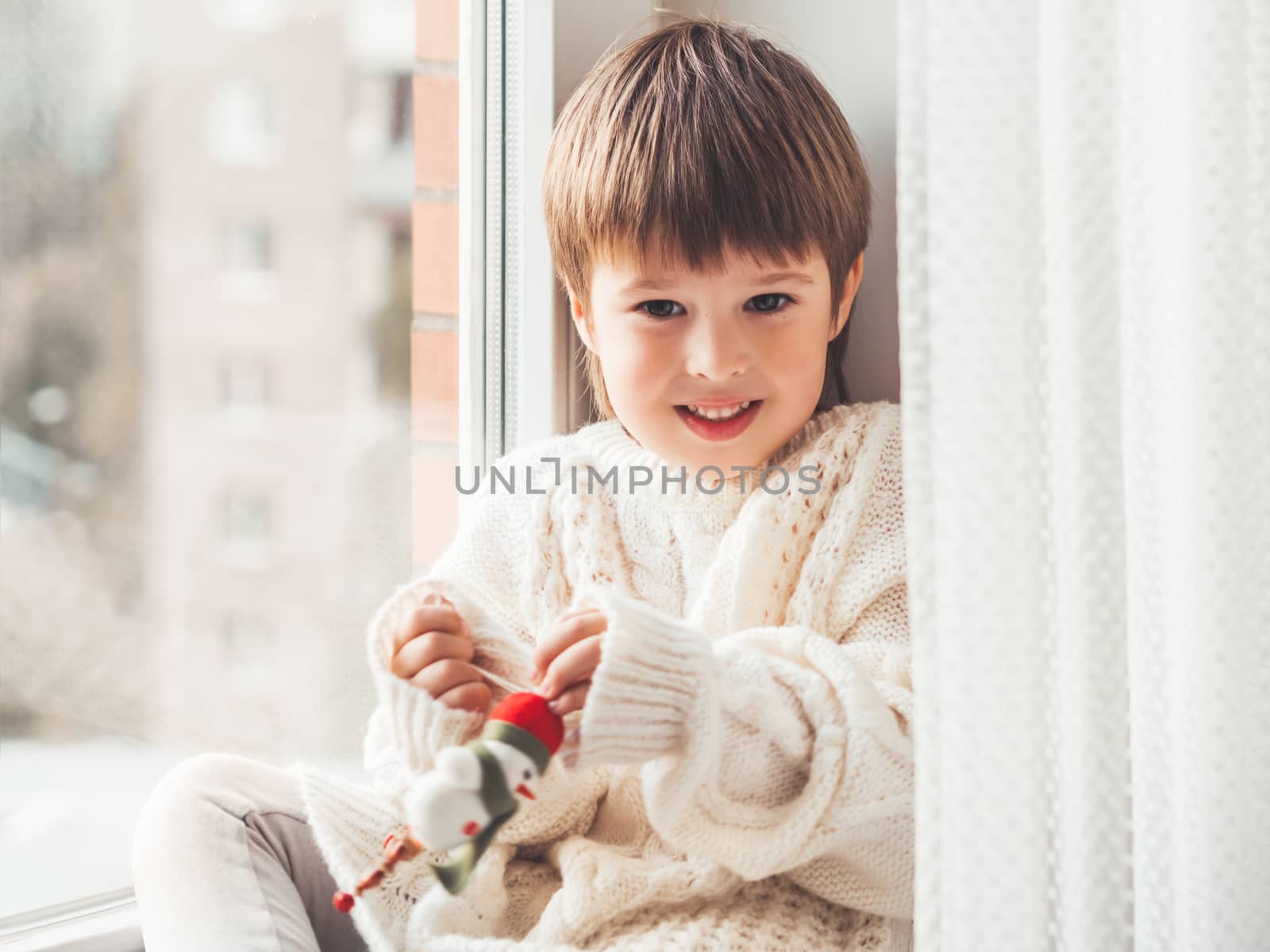 Kid with felt decorative snowman for Christmas tree. Boy in cabl by aksenovko