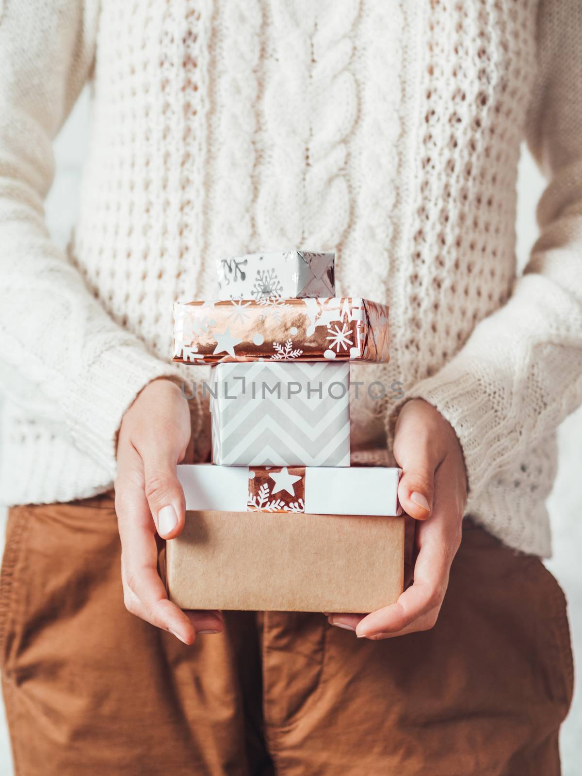 Woman in cable-knit white sweater with Scandinavian pattern and brown chinos trousers. Stack of Christmas presents in hands. Casual outfit for New Year celebration.