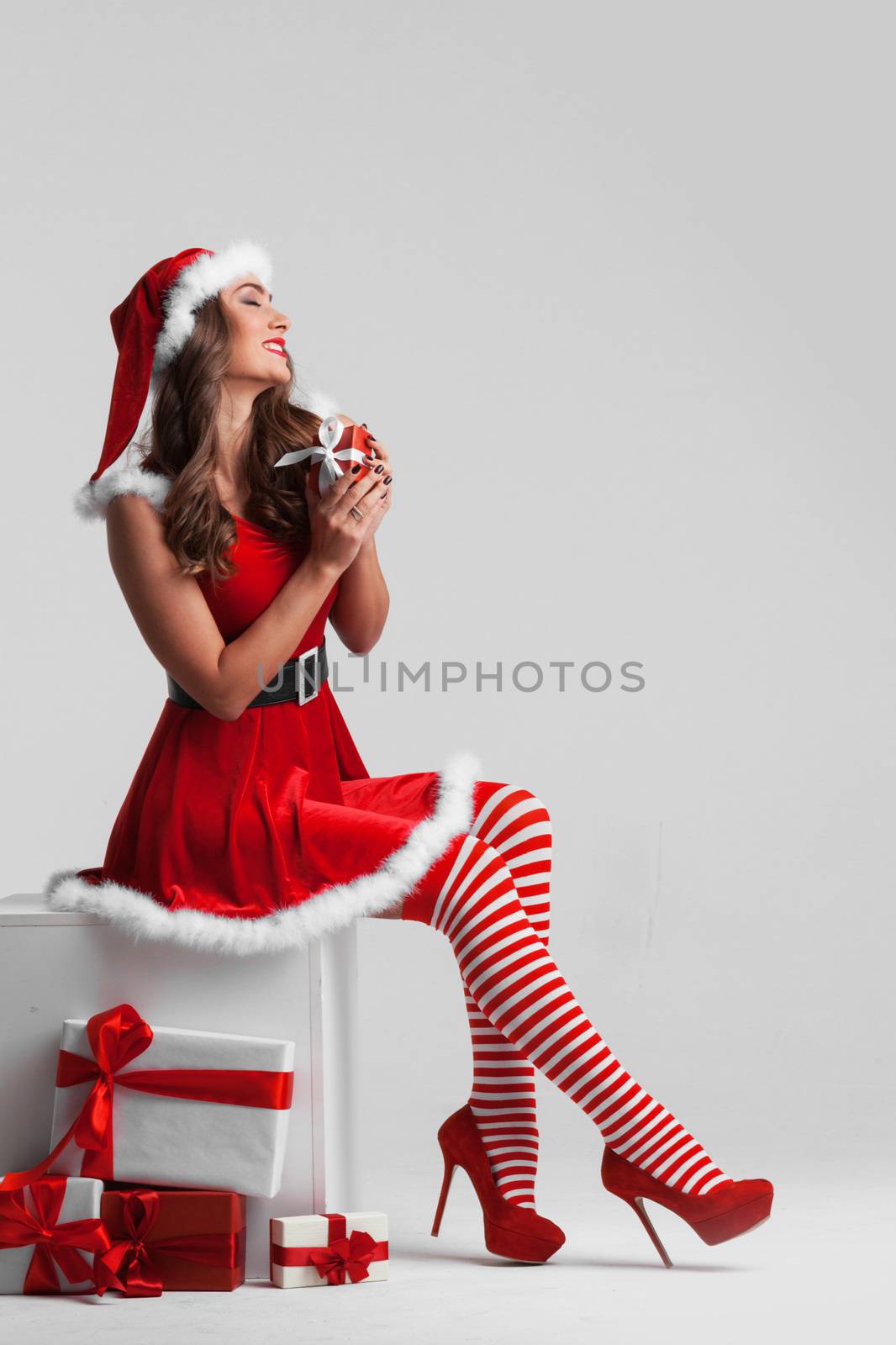 Beautiful Christmas pinup girl in red Santa dress and striped stockings with gift boxes