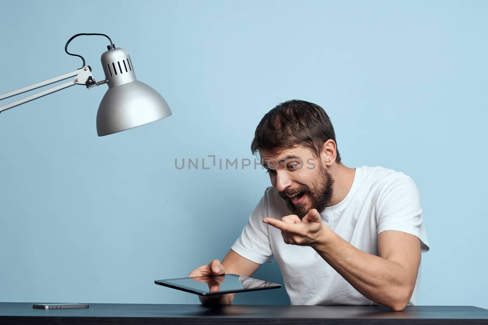 Man with tablet at table indoors and lamp work office freelancer blue background by SHOTPRIME