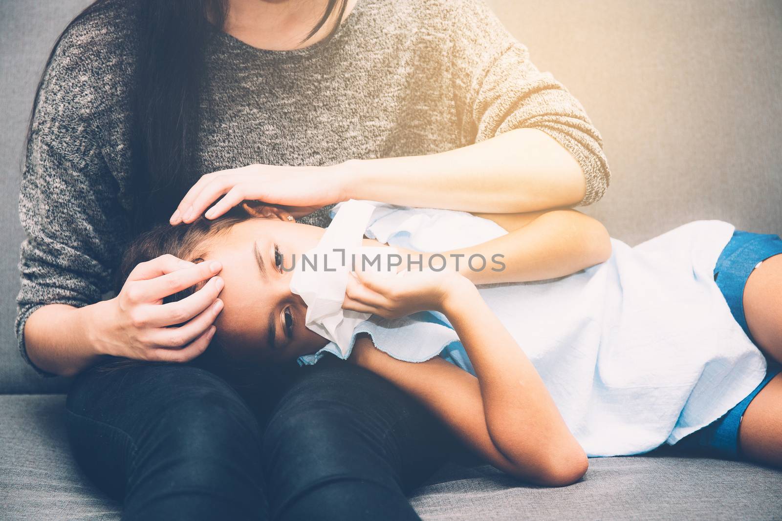 Little asian girl is sick weak lying on sofa with mother of take care and touching forehead in living room - family health concept.
