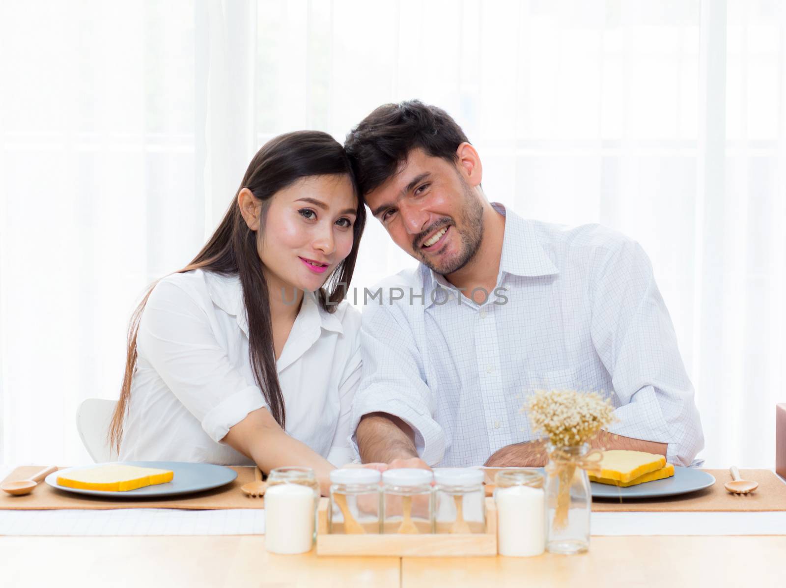 Cheerful asian young man and woman having sitting lunch and talking together at kitchen, family relationship with romantic concept.