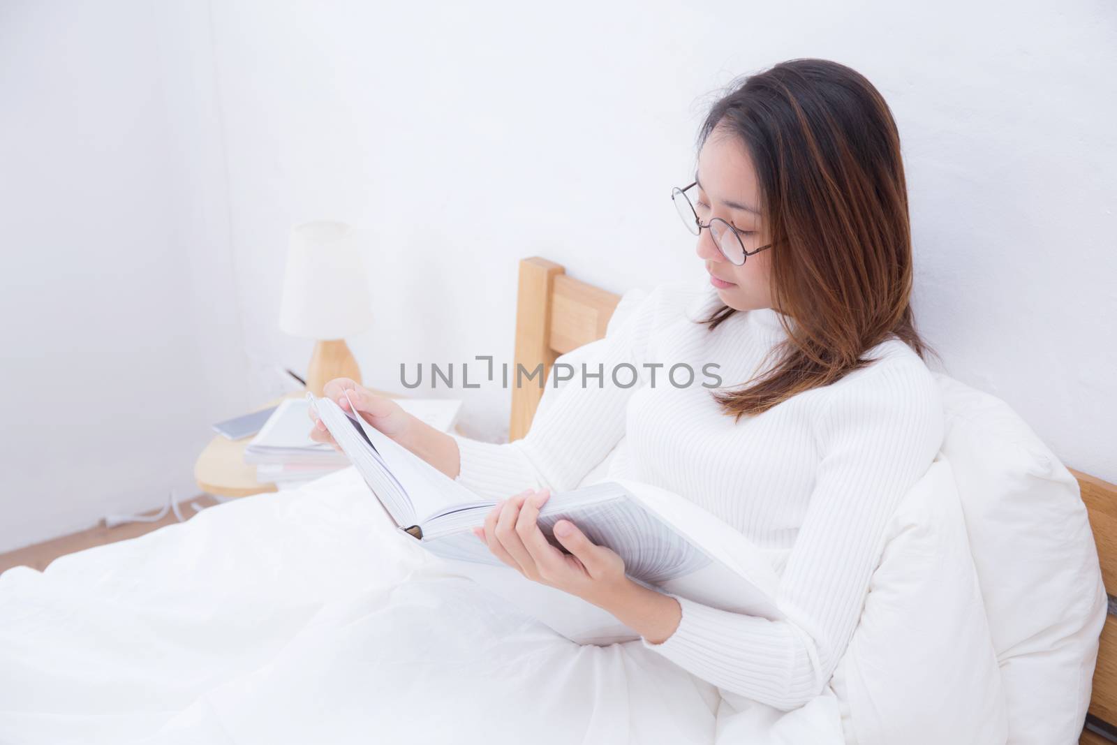 Beautiful young asian woman reading a magazine book in bedroom w by nnudoo