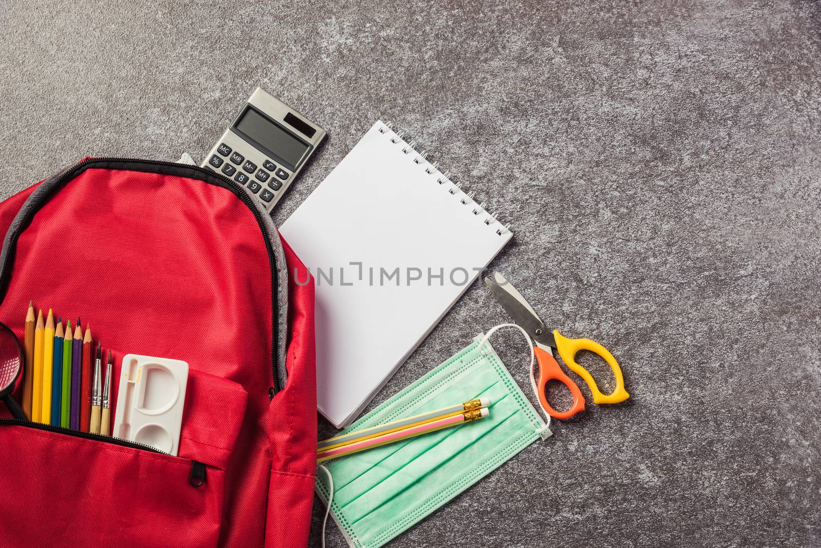 Top view of stylish red school bag backpack on a table desk with face mask protection and stationery, Back to school education new normal during outbreak COVID-19 or coronavirus concept