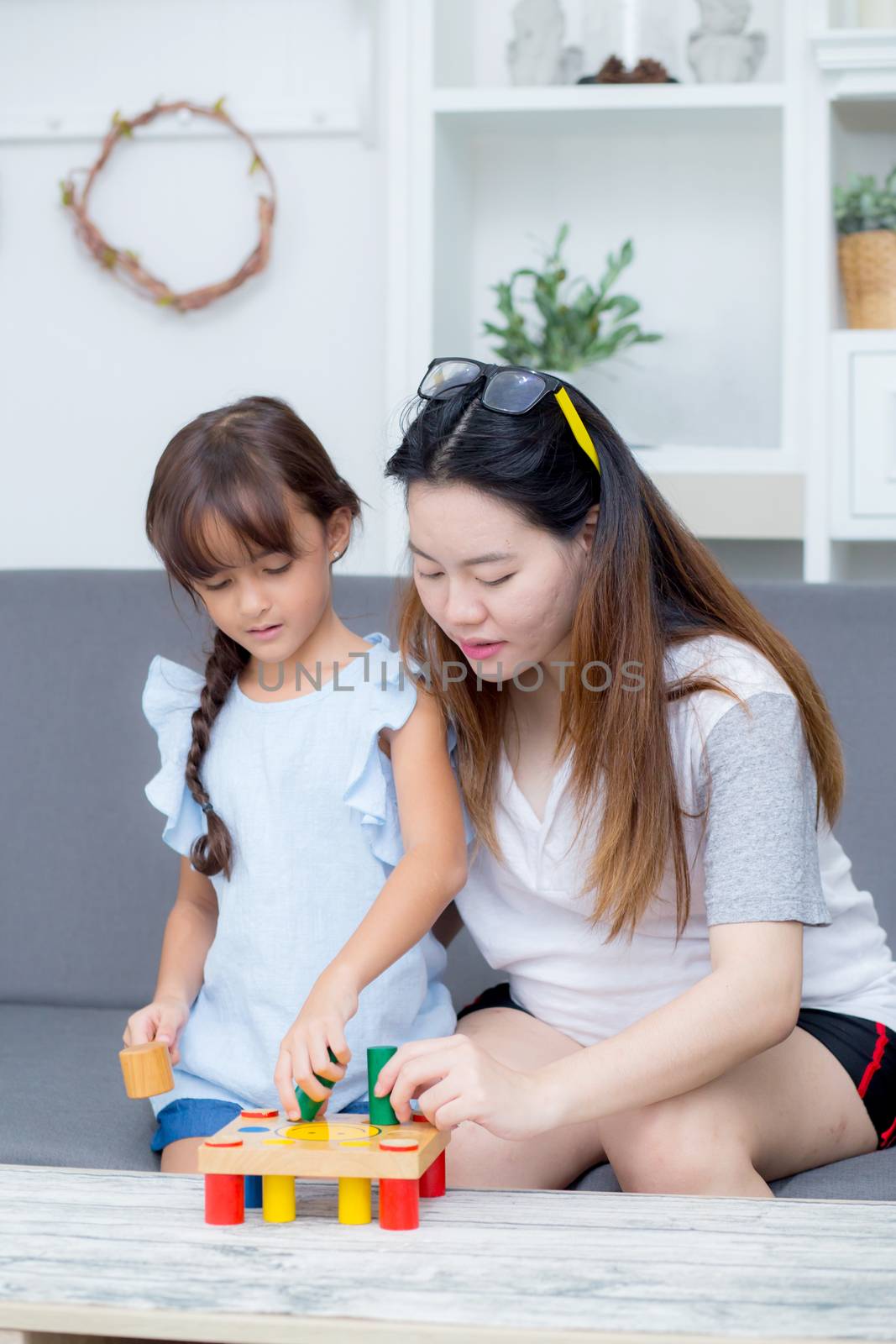 Asian kid girl and mother playing toy block; together with cheerful and happy in living room, activity in family.