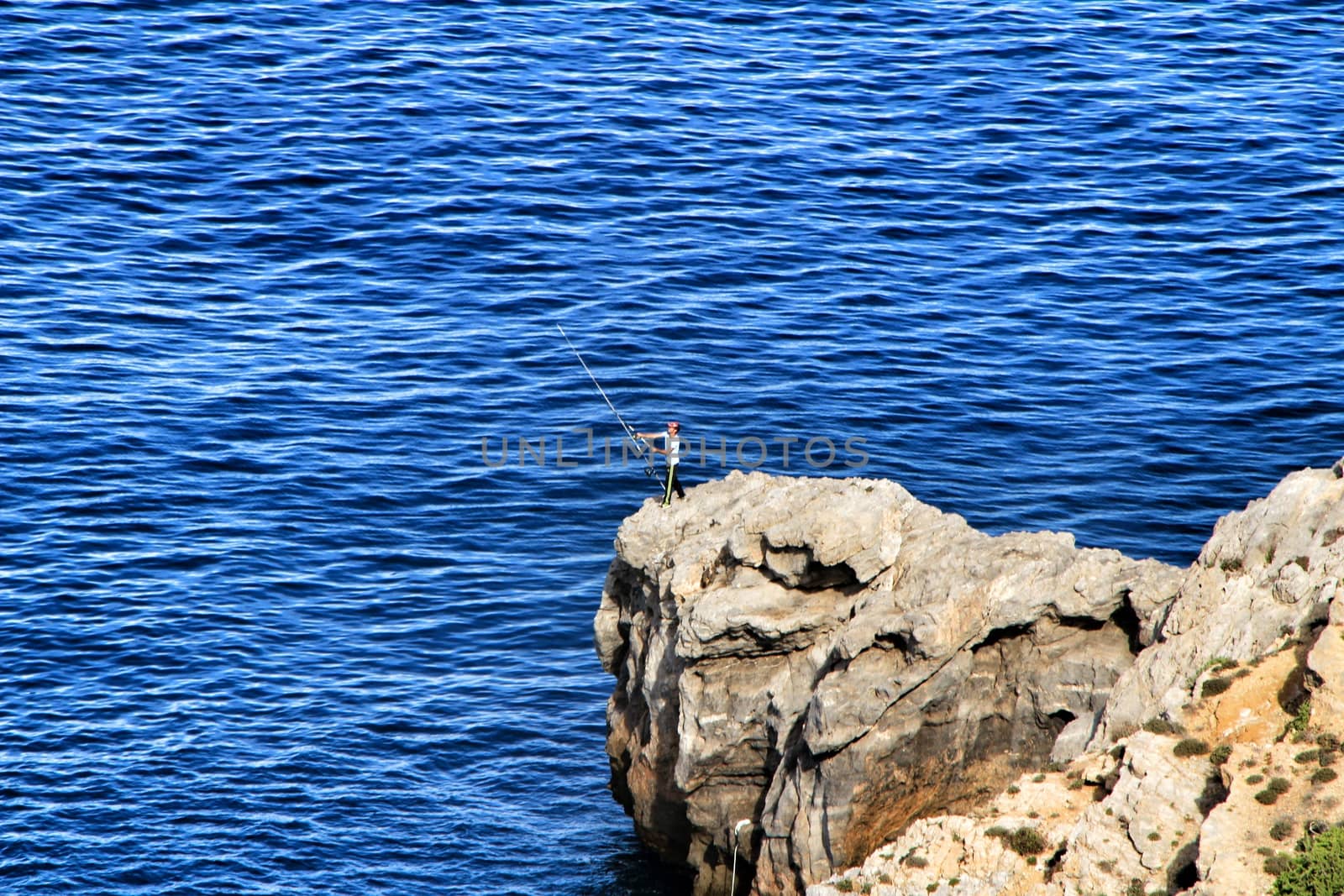 La Azohia, Murcia, Spain- October 2, 2019: Fisherman fishing on the rocks in the evening on La Azohia beach in a sunny day. Cartagena province, Murcia,Spain.