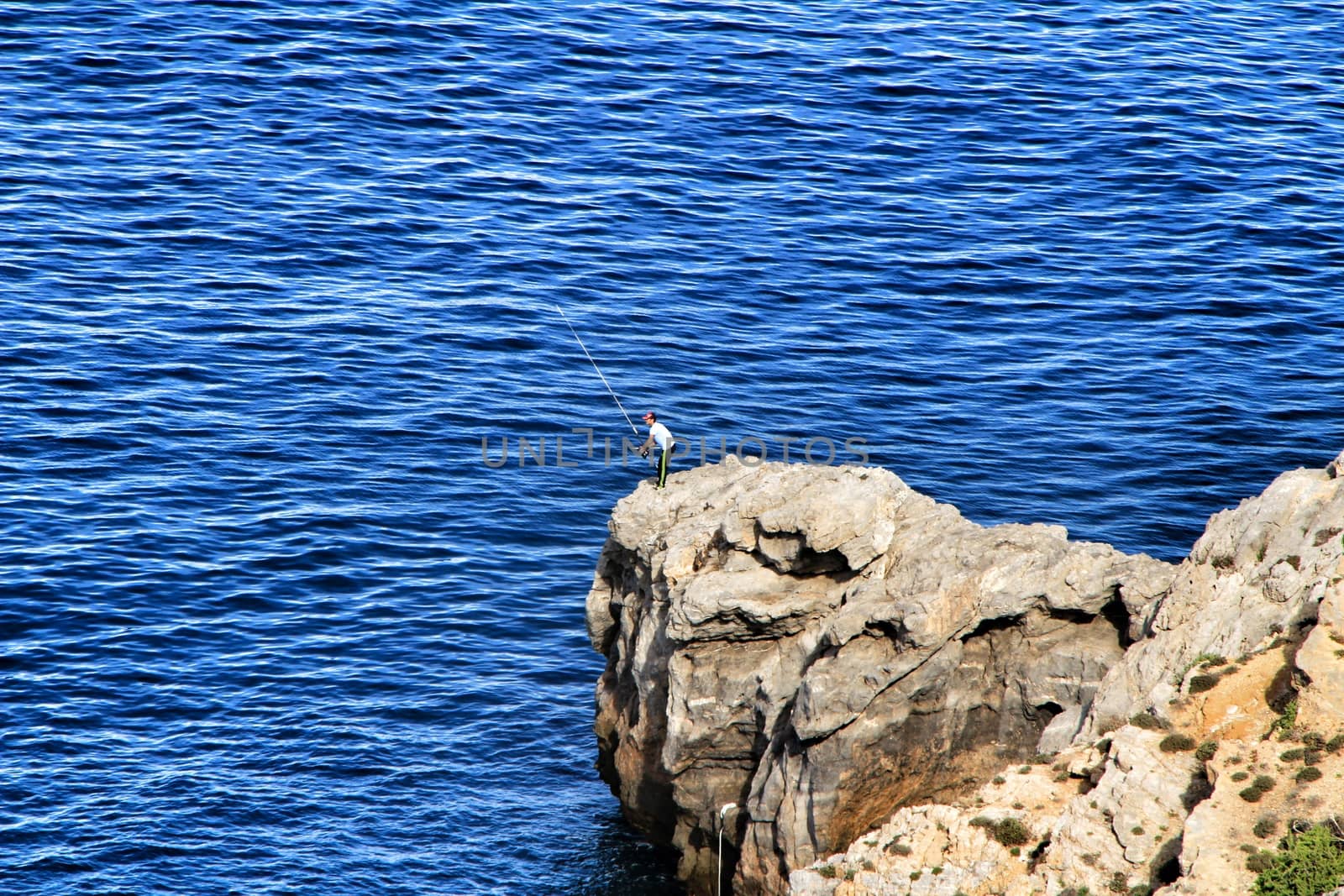 La Azohia, Murcia, Spain- October 2, 2019: Fisherman fishing on the rocks in the evening on La Azohia beach in a sunny day. Cartagena province, Murcia,Spain.