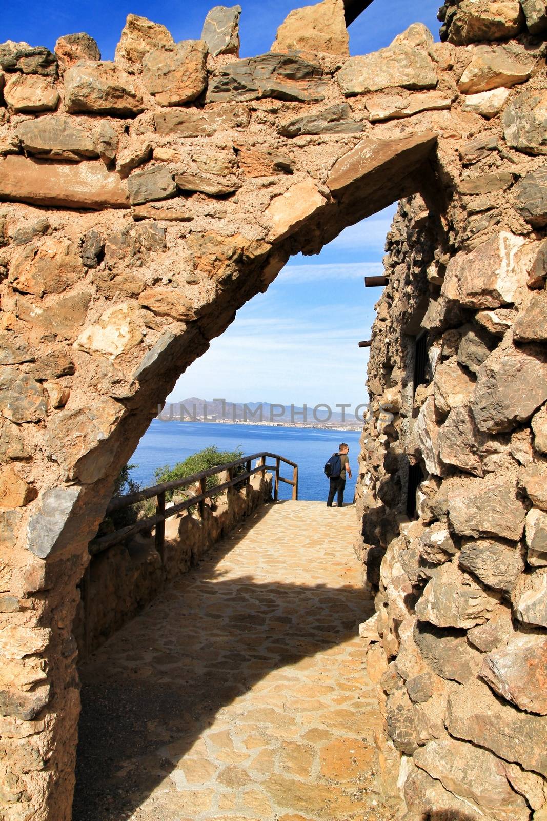 La Azohia, Cartagena, Spain- October 2, 2019: Tourist visiting and relaxing in Santa Elena tower in a sunny day of Autumn. Strong stone arch of Santa Elena tower in the foreground.