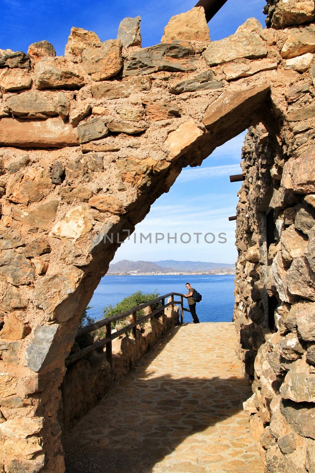La Azohia, Cartagena, Spain- October 2, 2019: Tourist visiting and relaxing in Santa Elena tower in a sunny day of Autumn. Strong stone arch of Santa Elena tower in the foreground.