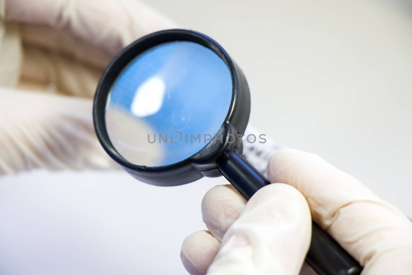 Magnifying glass and human hands with glove, looking and research something in Laboratory. by Taidundua