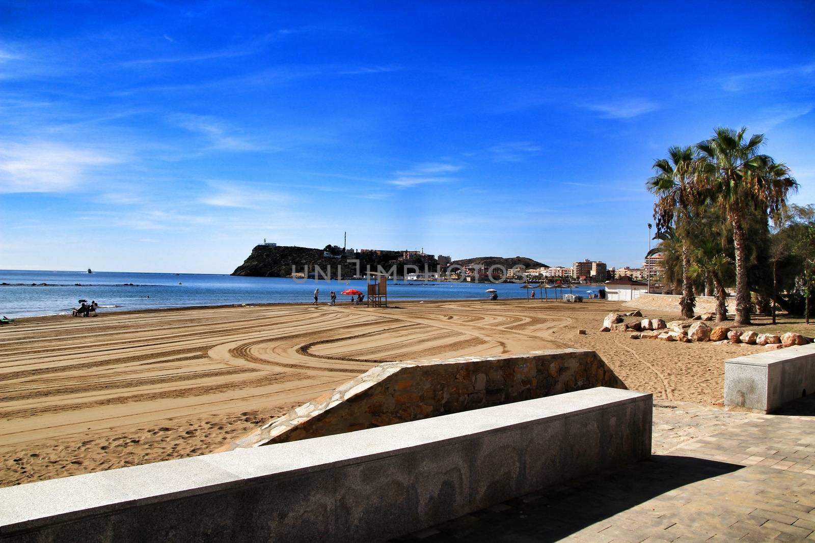 Mazarron, Murcia, Spain- October 3, 2019: Beautiful beach view from the promenade in a sunny and clear day in Mazarron, Murcia, Spain. People relaxing and sunbathing on the beach.