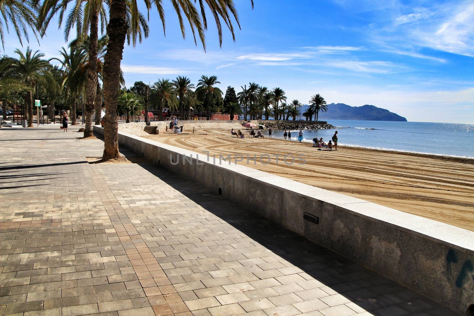 Mazarron, Murcia, Spain- October 3, 2019: Beautiful beach view from the promenade in a sunny and clear day in Mazarron, Murcia, Spain. People relaxing and sunbathing on the beach.