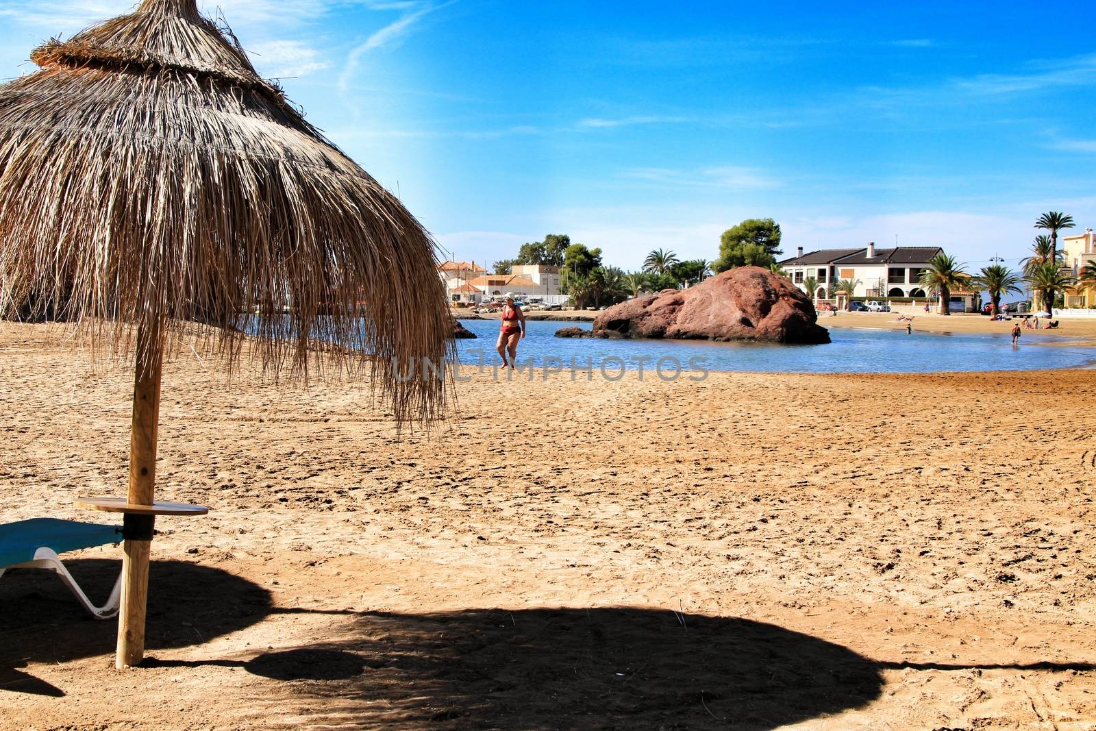 Mazarron, Murcia, Spain- October 3, 2019: People swimming and relaxing on the Beautiful Ermita beach in a sunny day in Mazarron, Murcia, Spain. Umbrellas and hammocks in the foreground.